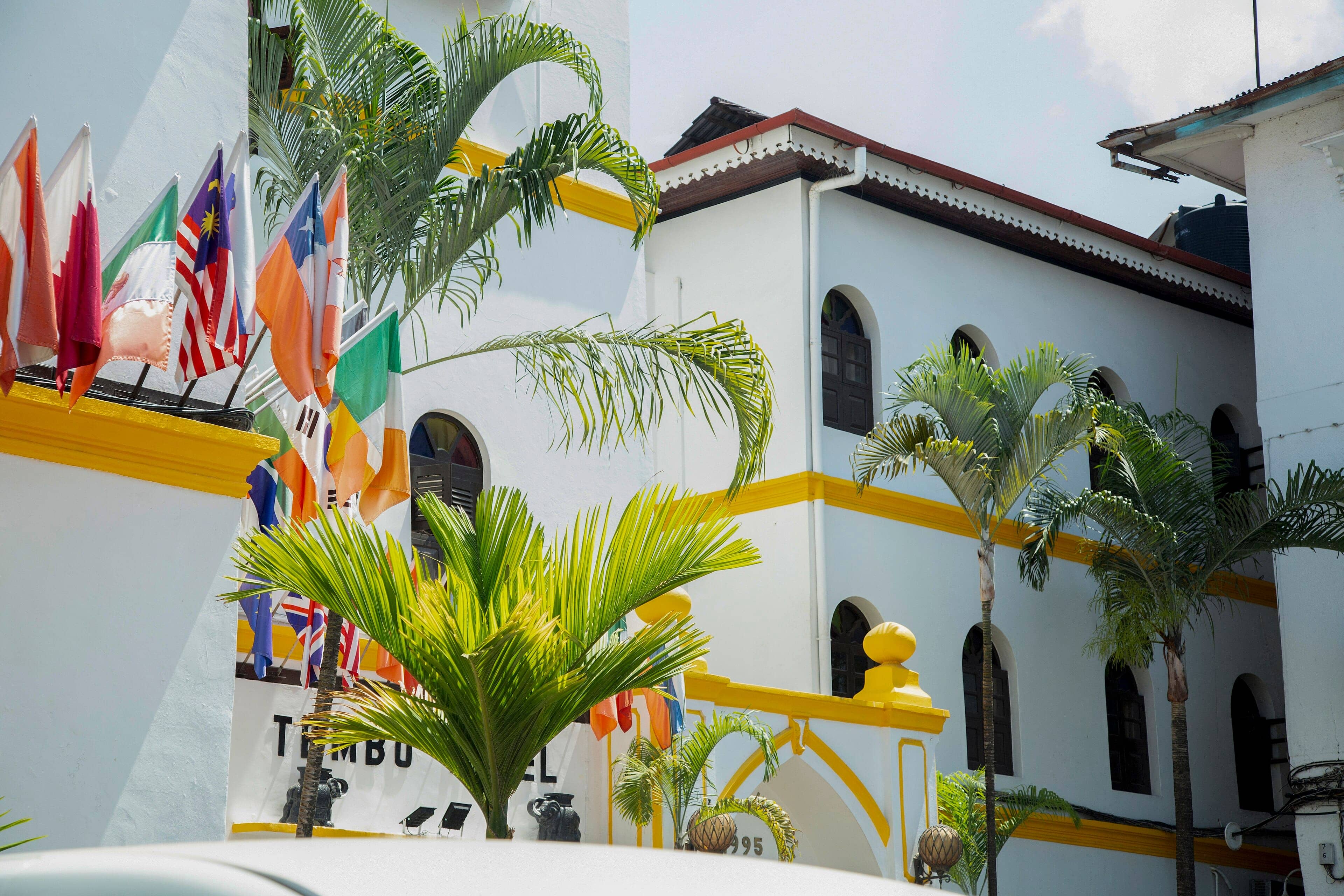 The white front of Tembo House Hotel on the Stone Town seafront, with palms and a row of flags